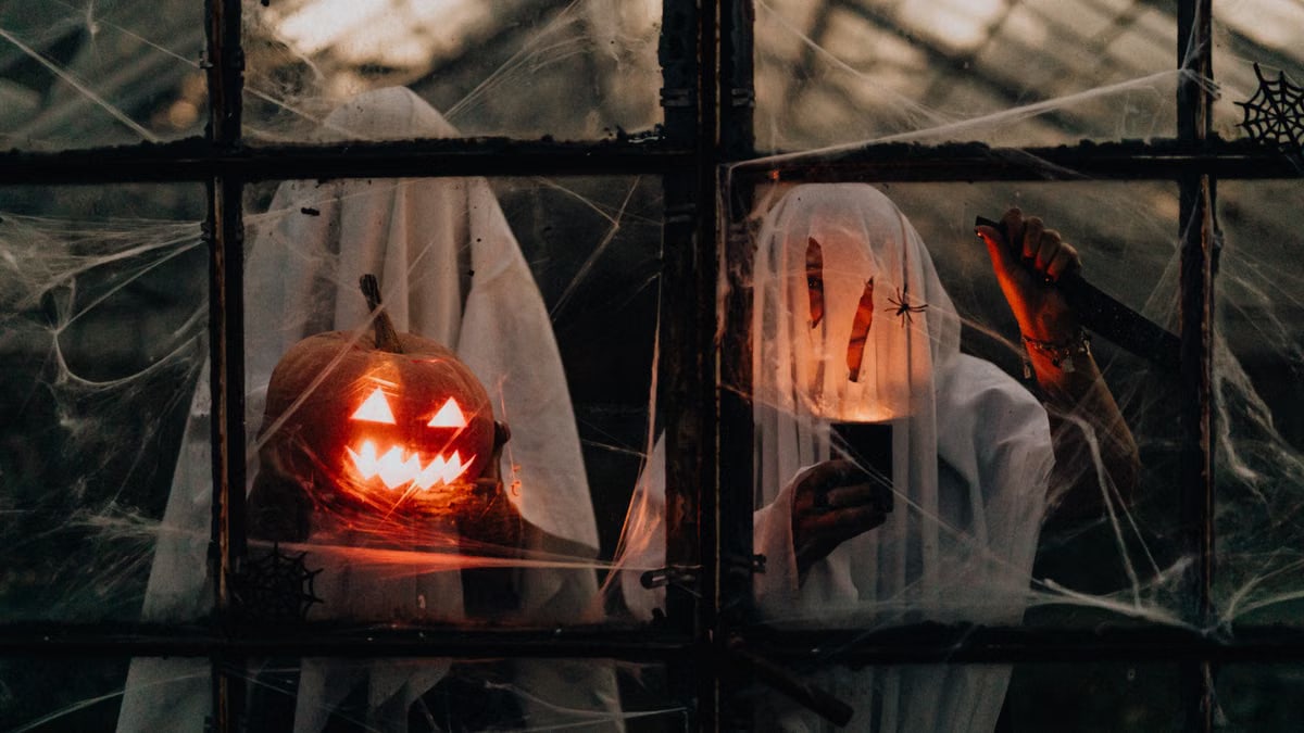 Eerie night shot of ghosts with jack-o'-lantern and cobwebs through a window, perfect for Halloween themes.